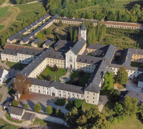 Aerial view of a large, historic monastery complex surrounded by lush greenery and fields, with a central courtyard and a serene, peaceful ambiance.