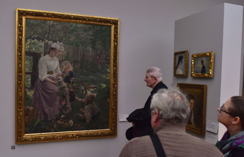 people admiring a art picture with woman with flowers in the summer and with the child near her