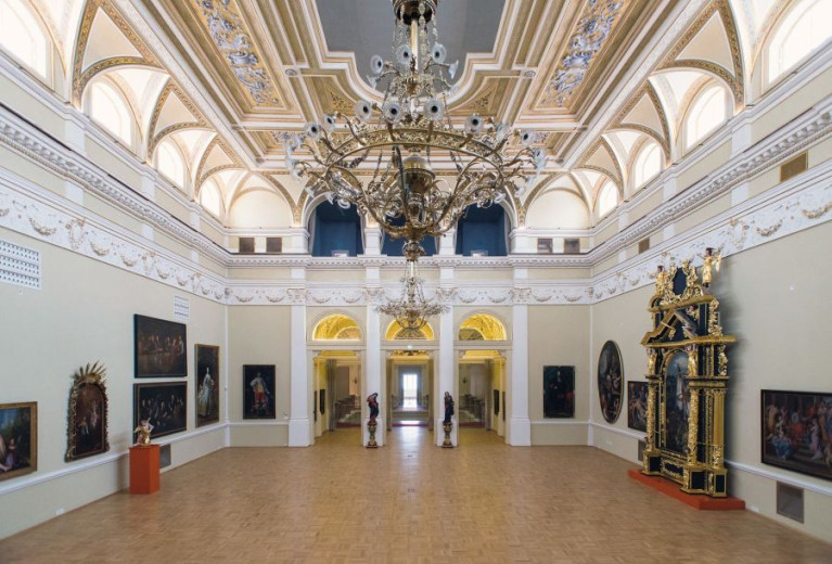 a big hall in gold and white with a lot of paintings on the wall