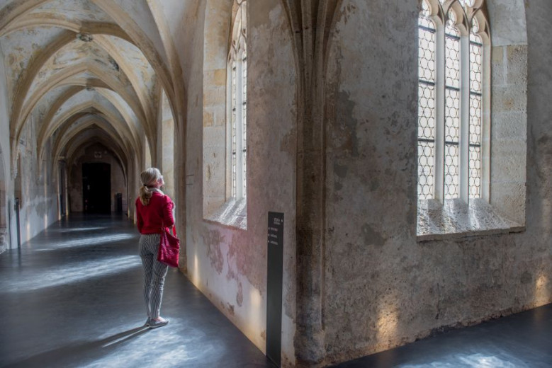 Visitor walking through a peaceful historic cloister with stone arches and soft light filtering through old windows.