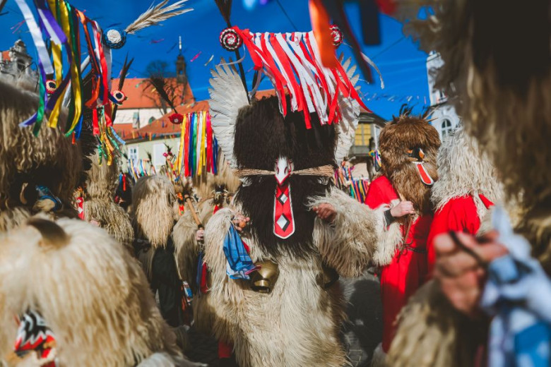 Kurents in fur costumes with tall ribboned headpieces and cowbells gathering for a vibrant traditional parade.