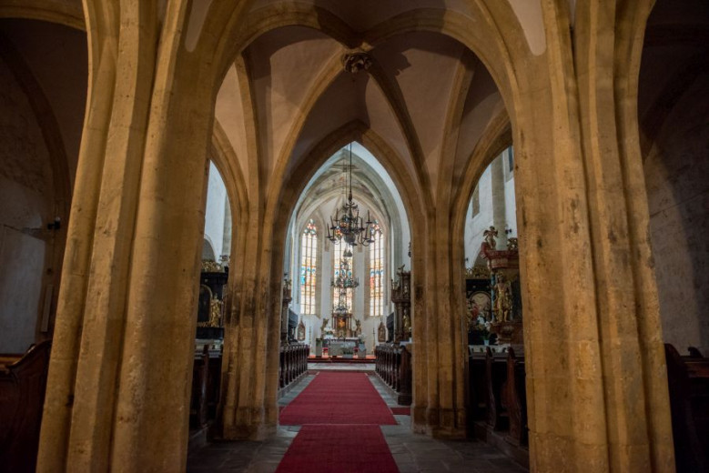 A quiet church interior with tall stone arches, wooden seats, and soft light shining through colorful stained-glass windows.