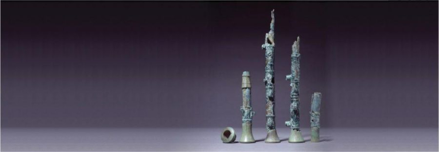 Ancient bronze fragments arranged upright resemble a type of Roman flute, showing delicate details of an old musical instrument preserved through time.