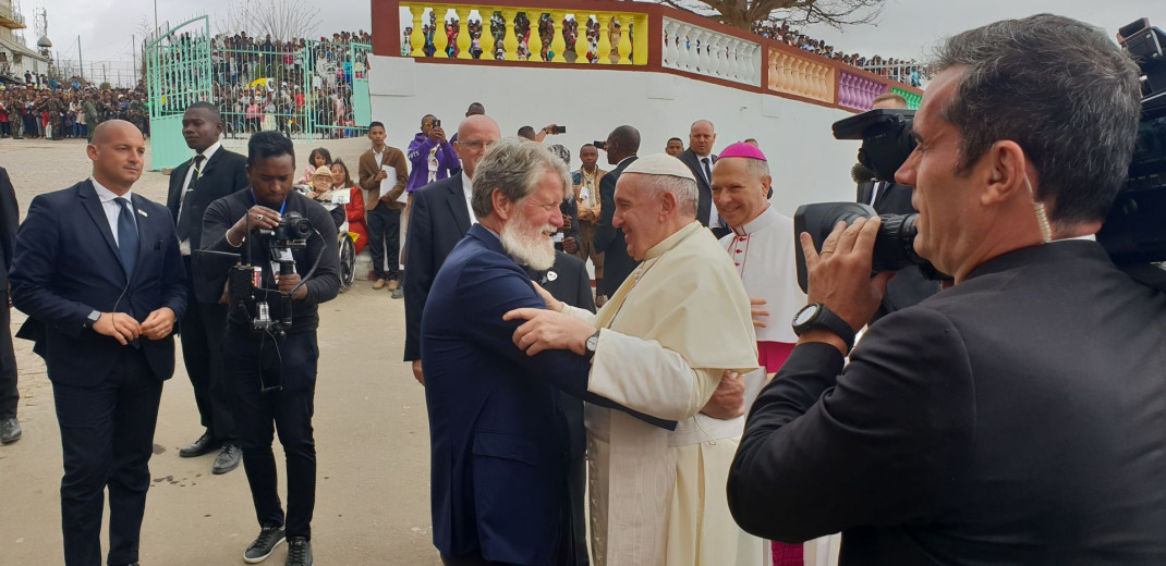 Pedro Opeka stoji in se pogovarja s papežem Frančiškom ob njiju pa so drugi prebivalci Madagaskarja. 