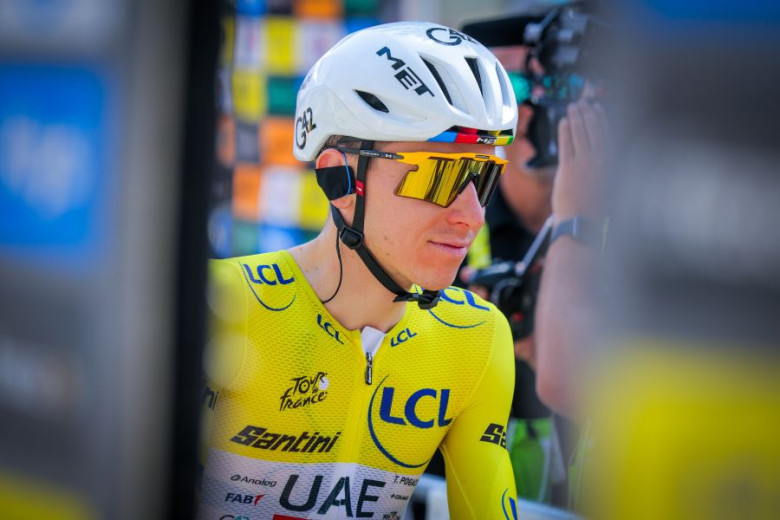 Tadej Pogačar in yellow jersey and helmet, wearing sunglasses, in profile at a race. 