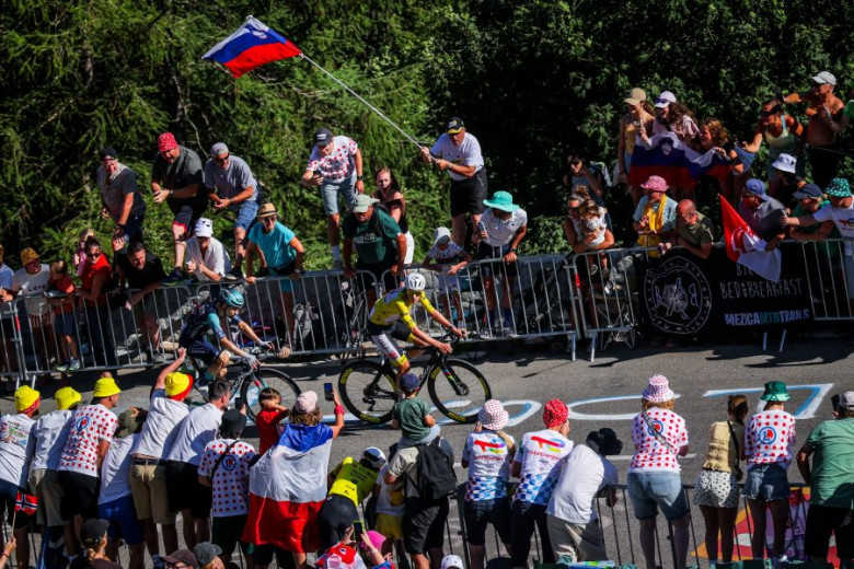 Tadej Pogačar in a race ascend a hill, surrounded by enthusiastic spectators. 