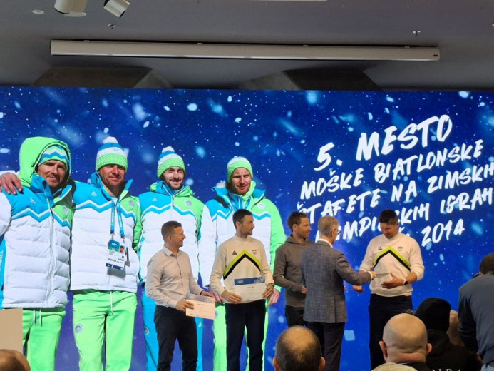 Pet športnikov v zeleno-belih bundah stoji na odru ob podelitvi priznanj, v rokah držijo plakete, za njimi je zimsko ozadje.