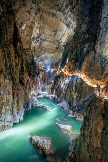 A deep cave gorge with flowing water and a narrow wall path reveals an impressive underground space to visitors.