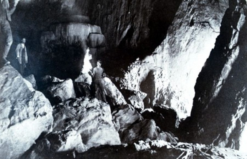 An old cave photograph shows explorers among rocks, lit faintly by torchlight.