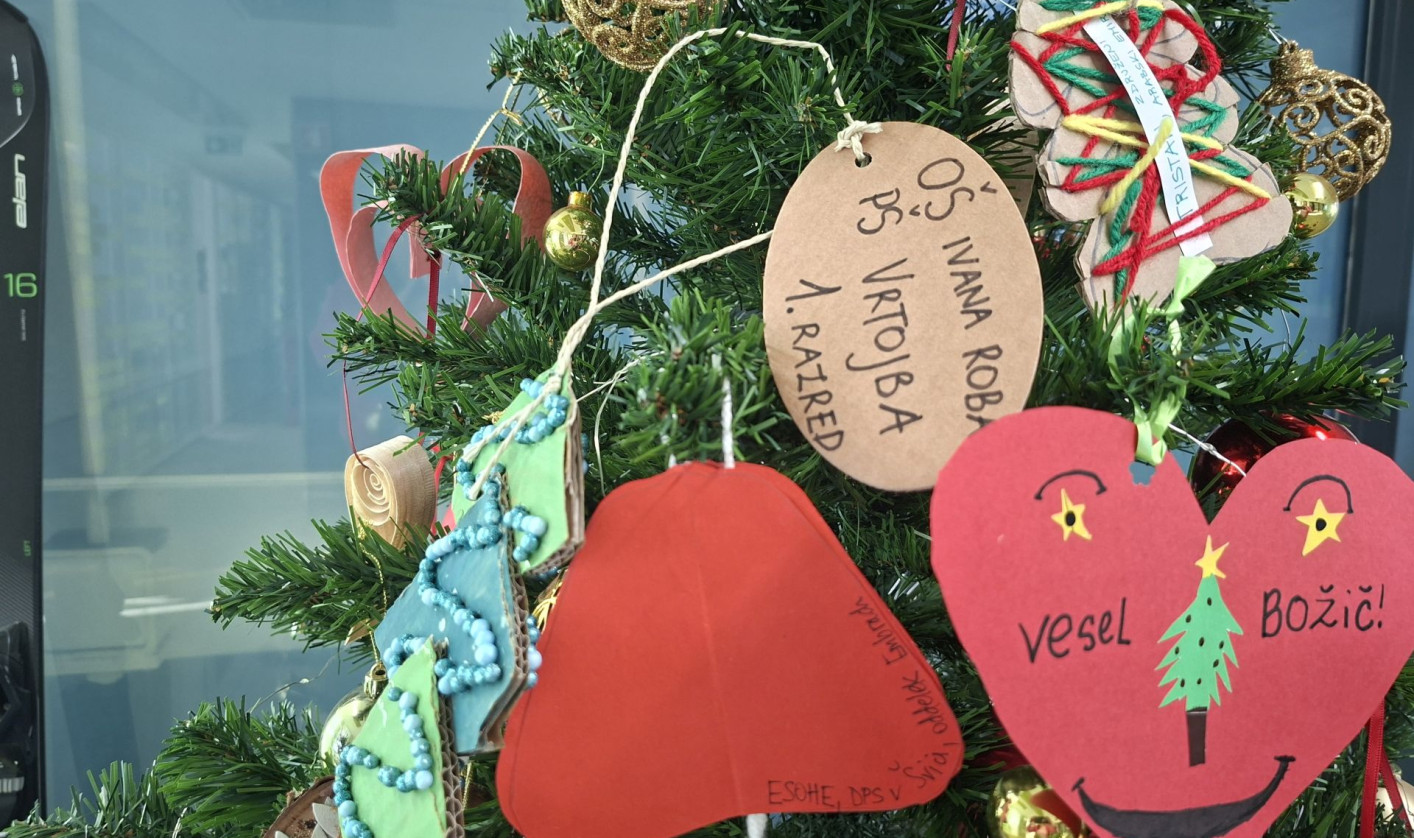 Christmas tree decorated with handmade paper hearts, wooden tags, and colorful ornaments hanging among green branches.