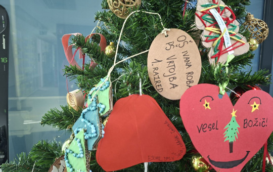 Christmas tree decorated with handmade paper hearts, wooden tags, and colorful ornaments hanging among green branches.