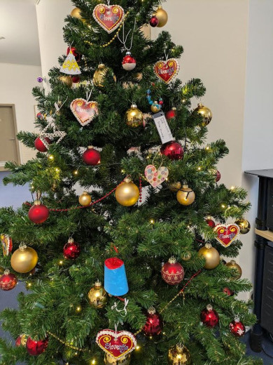 Okrašeno božično drevo z rdečimi in zlatimi okraski, okraski iz medenjakov v obliki srca in toplimi belimi lučkami v notranjosti.