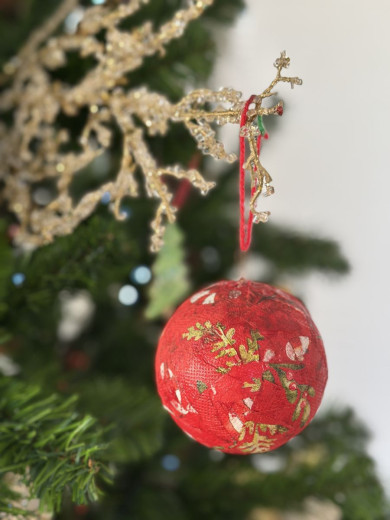 Bližnji posnetek rdeče božične kroglice z zlatimi vzorci, ki visi na veji božičnega drevesca.