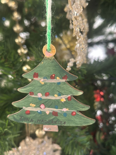 Ročno poslikan lesen okrasek božičnega drevesa v zeleni barvi z barvitimi pikami, ki visi na božičnem drevescu.