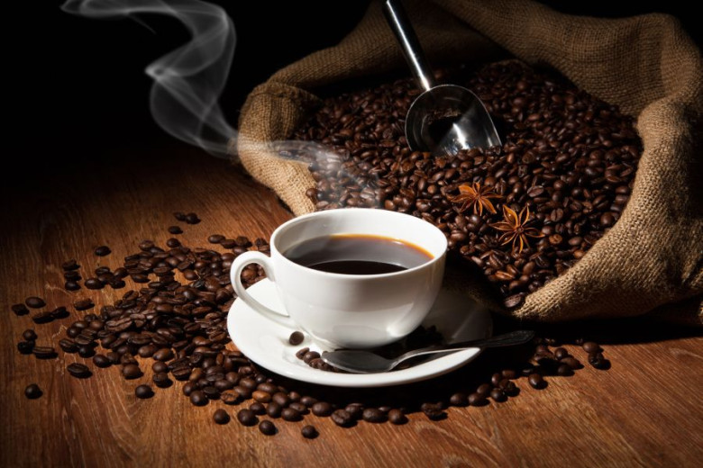 A cup of coffee on the wooden table and spilled coffee beans around the cup