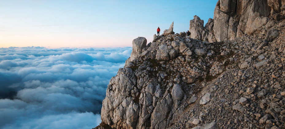 Rocky mountain ridge high above the clouds in the Julian Alps, with a clear blue sky in the background.