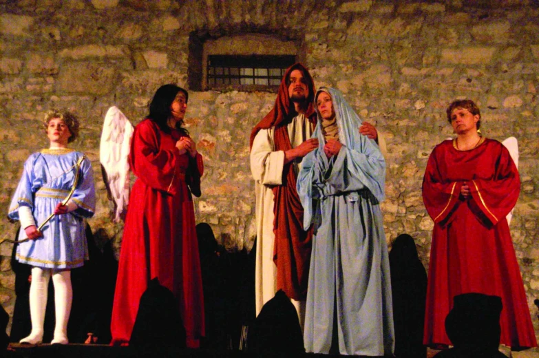 On the stage are actors, dressed in Mary and Joseph, holding each other, and angels are standing near. 