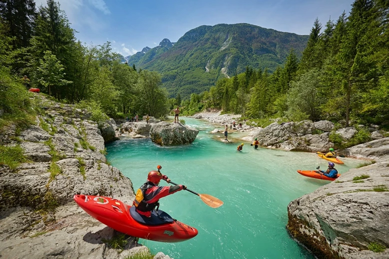 Kayakers paddling on the emerald-green Soča River, surrounded by Alpine scenery and forested mountains.