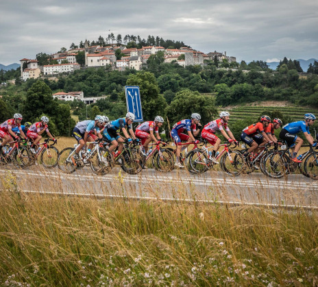 A group of cyclists on the road and a town on a hill in the background.