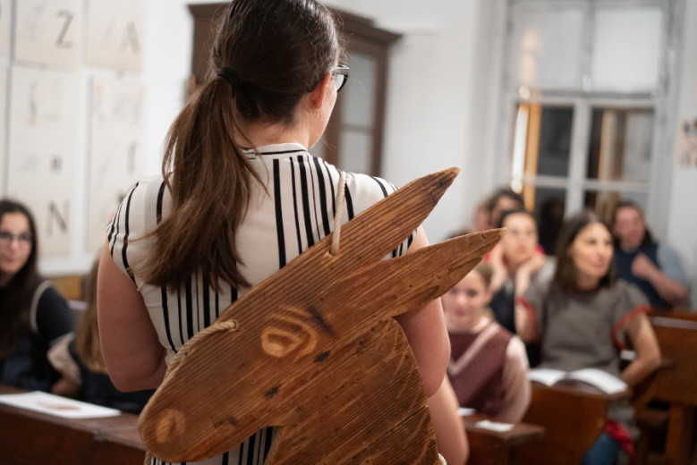 Visitor wearing a traditional wooden donkey sign in a reconstructed historical classroom in Slovenia.