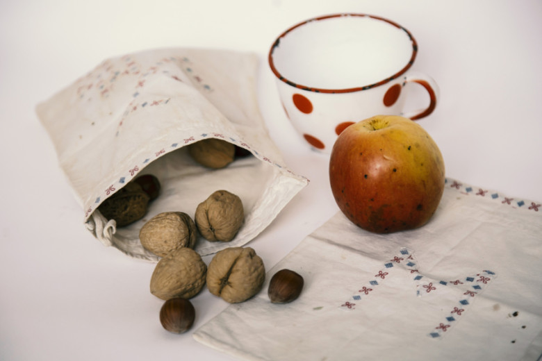 Slovenian school snack with an apple, walnuts, hazelnuts, and an enamel mug with red dots.