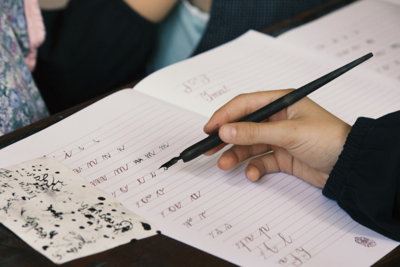 Hand writing in a notebook with a metal dip pen during a calligraphy lesson.