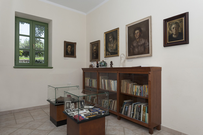 Interior of a room with portraits on the wall, a glass display case and a bookcase.