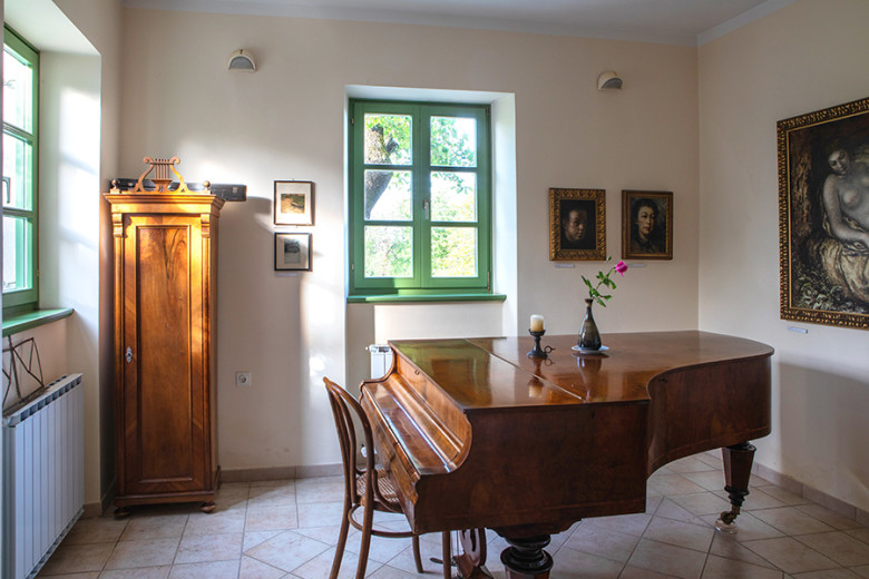 Interior of a room with a grand piano, wooden wardrobe and framed paintings.