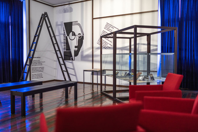 Exhibition room with a ladder, glass display case and a graphic portrait of a poet on the wall.