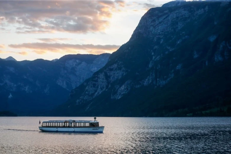 A tourist boat floating on the Bohinj lake, hills and cloudy sky in the background. 