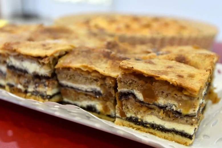Pieces of a dessert with layers of walnut filling, poppy seeds, apple filling, and cottage cheese filling, served on a plate. 