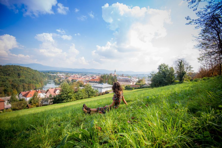 The girl is sitting on the grass. View of Novo mesto.