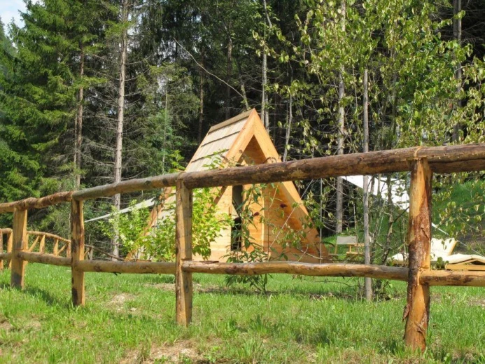 A wooden glamping tent behind a wooden fence, and a forest behind it. 