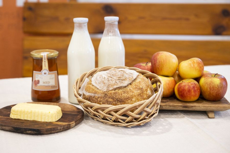 Med, dve steklenici mleka, kruh, maslo in jabolka na mizi.