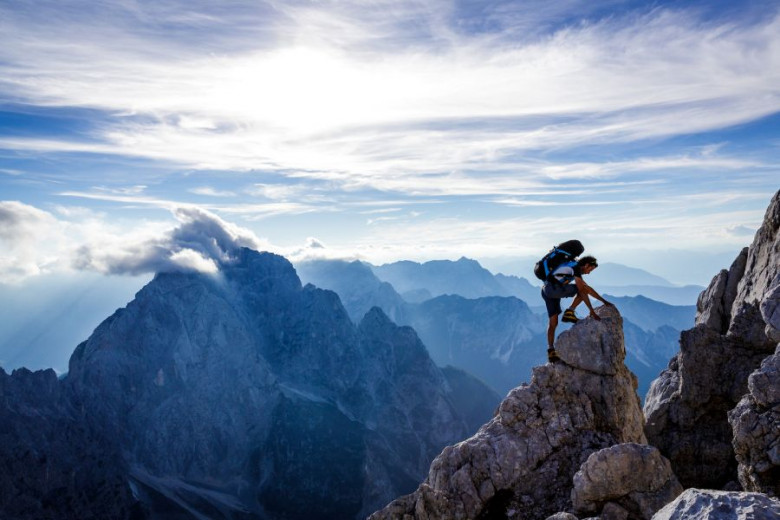A climber at the top of a steep mountain. View of mountains in the clouds.