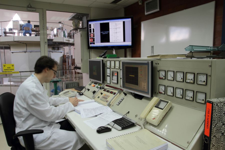 A researcher is sitting in the control room of the TRIGA reactor, with screens and buttons in front of him.