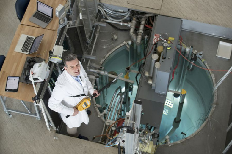 Scientist Luka Snoj standing above the TRIGA research reactor while holding a scientific measuring instrument.
