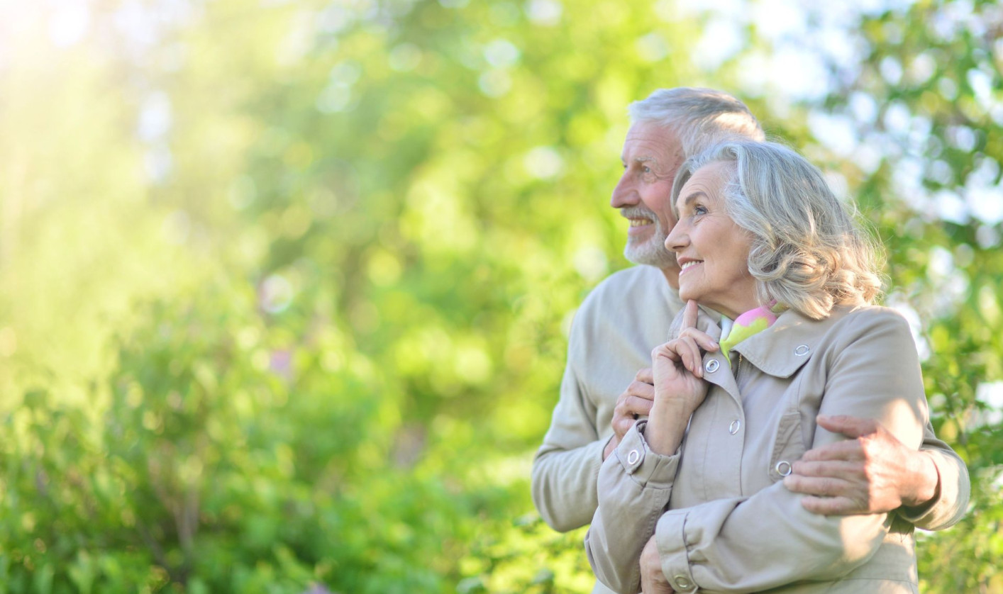 An older couple is hugging and smiling in green nature.