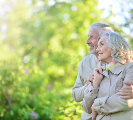 An older couple is hugging and smiling in green nature.