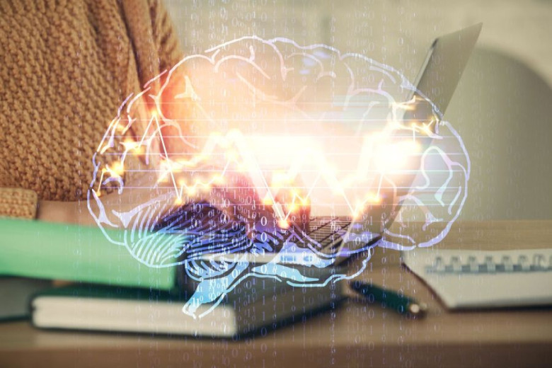Close-up of person using laptop with a luminous, semi-transparent drawing of a human brain.