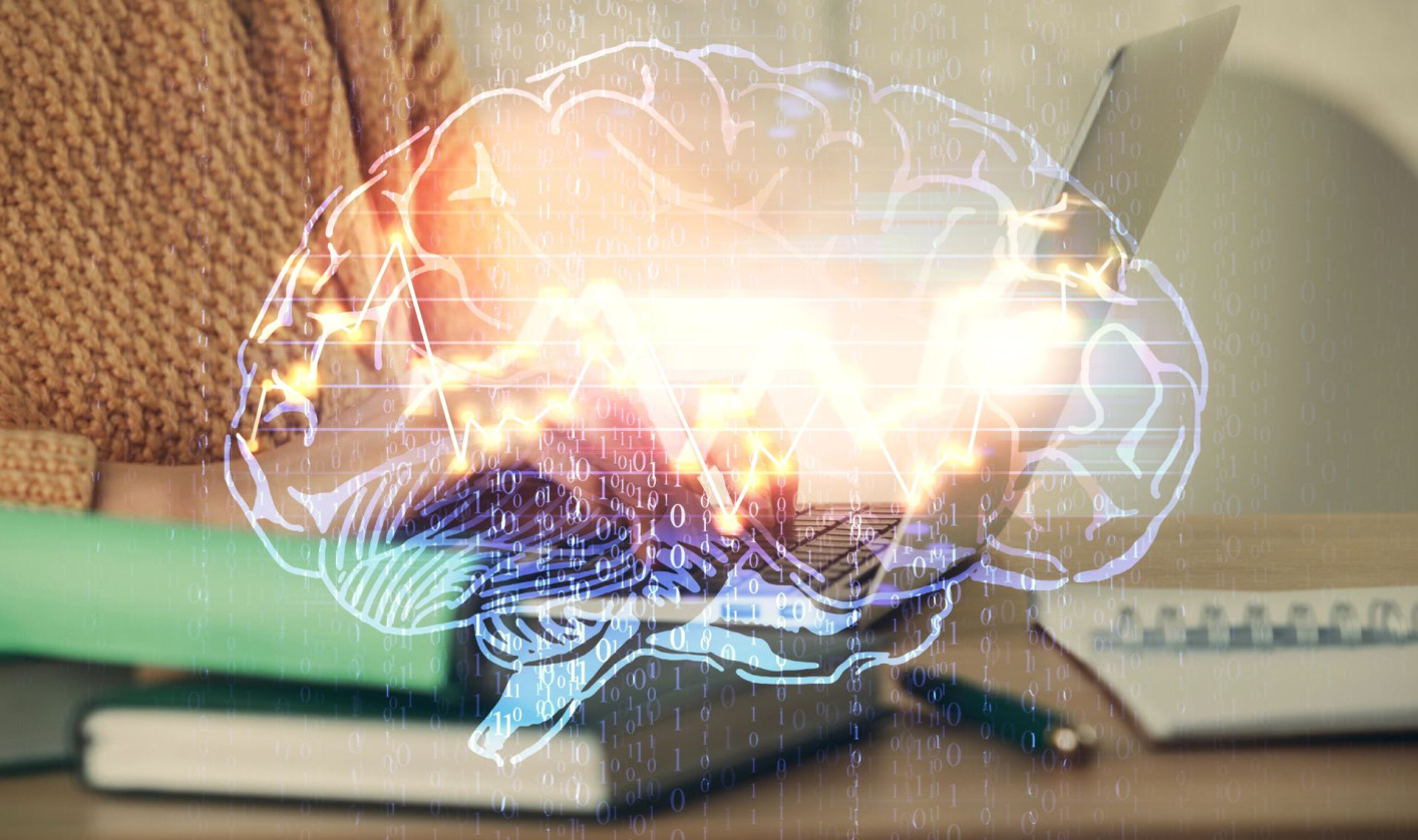 Close-up of person using laptop with a luminous, semi-transparent drawing of a human brain..