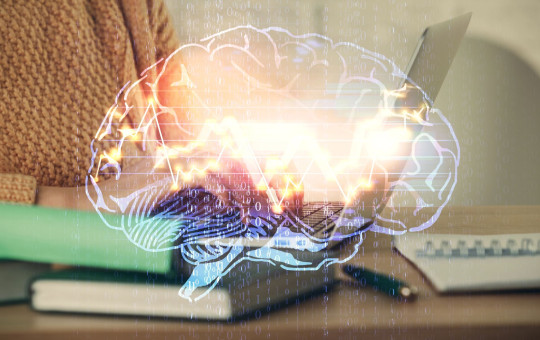 Close-up of person using laptop with a luminous, semi-transparent drawing of a human brain..