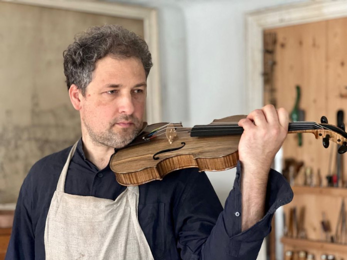 Violin maker Daniel Musek holds violin under chin in a workshop. 