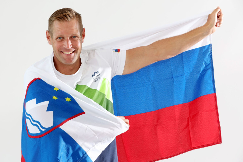 An adult man has in hands Slovenian flag in white, blue, red colour with the national emblem of  the mountain Triglav, sea and stars