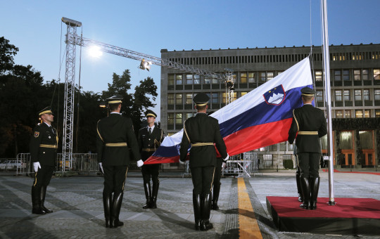 Pripadniki častne straže sodelujejo pri dvigu slovenske zastave na drogu na Trgu republike pred stavbo parlamenta.