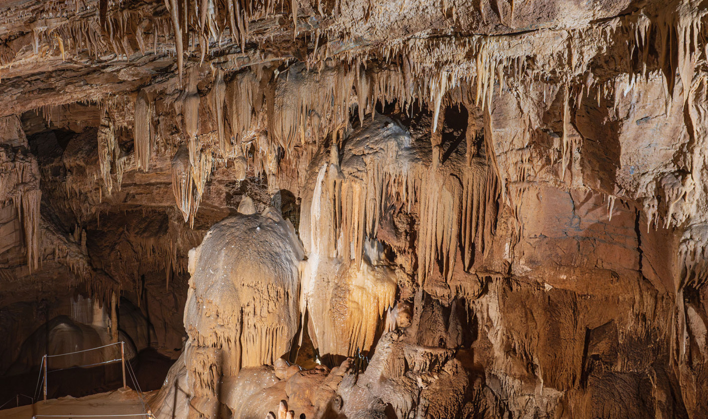 Stalactites and other cave formations of various shapes cover the ceiling and walls of a cave chamber.