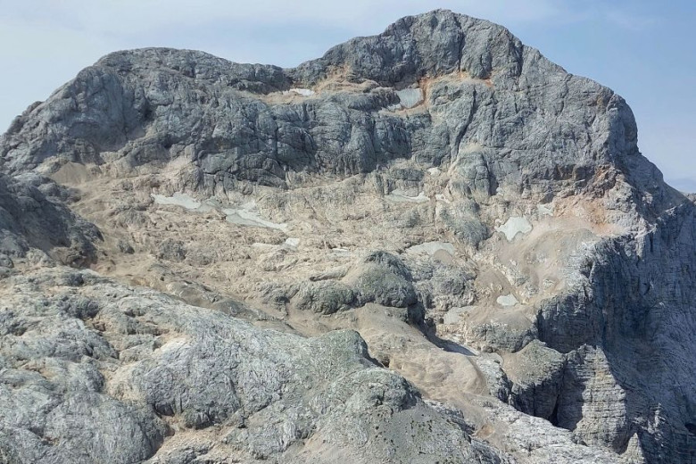 Grey mountain slope with barely visible patches of snow.