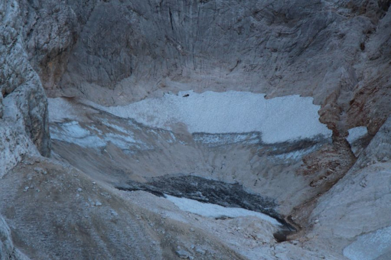 Photo showing a small mountain valley partially covered with snow.