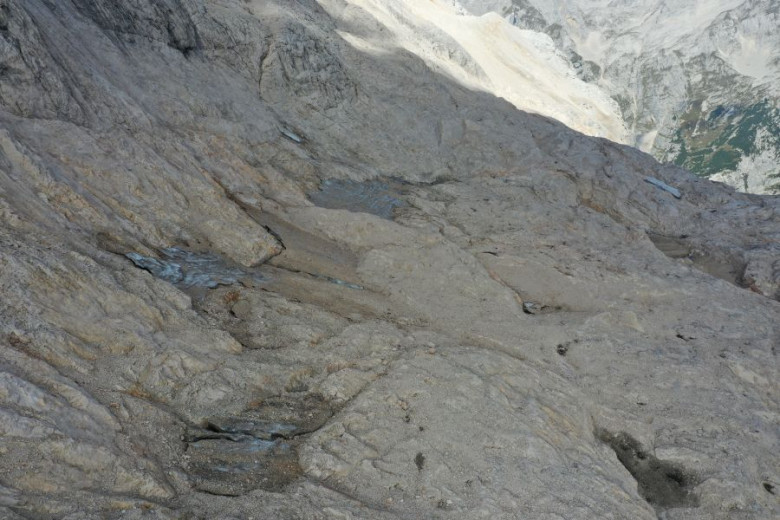 A grey mountain slope with small patches of ice.