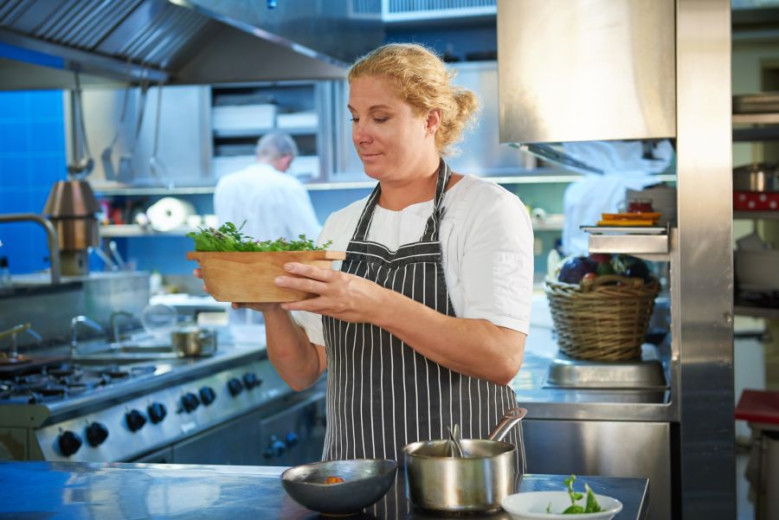 Ana Roš holds a bowl of vegetables in the kitchen. 